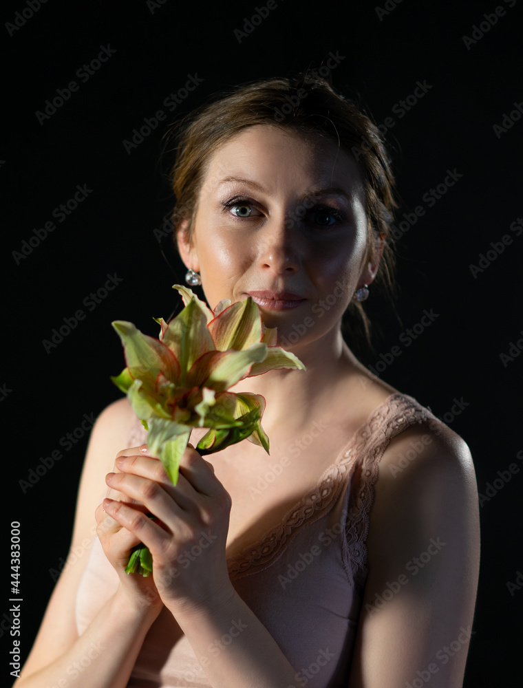 portrait of a woman with a flower. the girl looks at us and holds a plant in front of her. Black background. close-up portrait of a woman with a flower. the girl looks at us and holds a plant in front of her. Black background. close-up