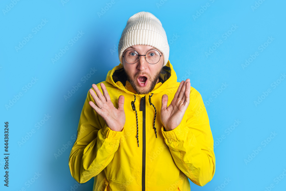 Surprised shocked bearded young man with glasses in a yellow jacket on a blue background Surprised shocked bearded young man with glasses in a yellow jacket on a blue background