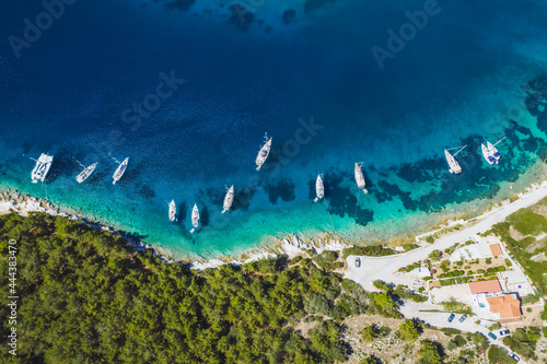 Top down aerial view of sailing boats docked in blue bay of Fiskardo, Kefalonia island, Ionian, Greece