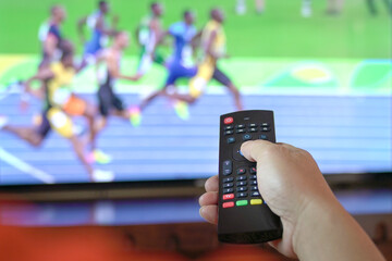 Man watch sports track and field on tv. Close up view on remote control.