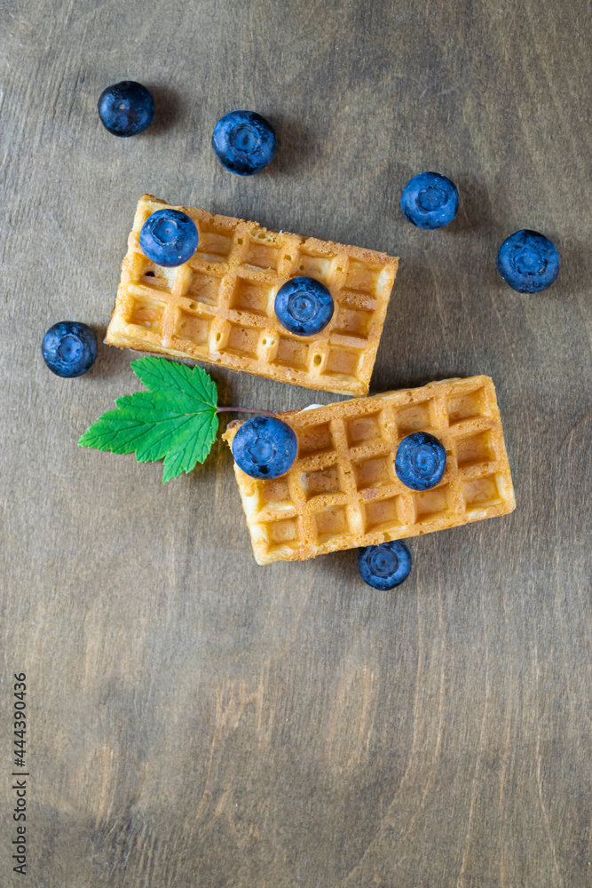 Soft Belgian waffles with blueberries on the background of a brown wooden table with a natural pattern, top view, copy space Soft Belgian waffles with blueberries on the background of a brown wooden table with a natural pattern, top view, copy space