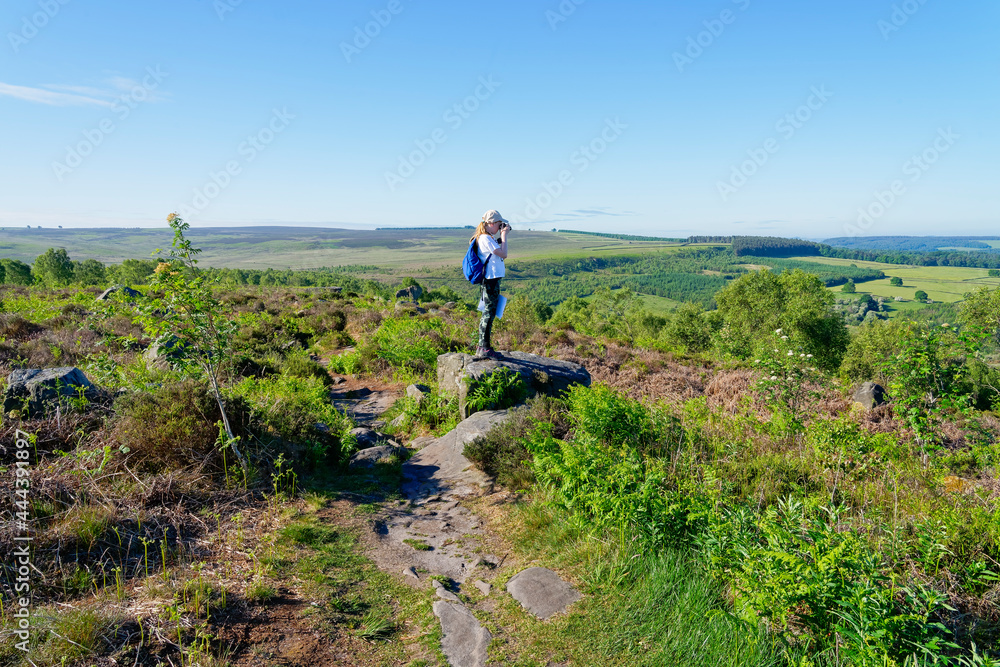 Young girl standing on a rock on Birchen Edge in the Derbyshire countryside taking pictures of the landscape