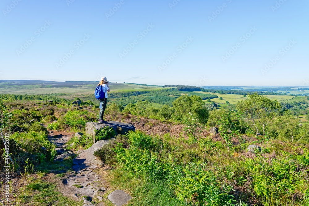 Young photographer standing on a rock on Birchen Edge taking photographs of the Derbyshire countryside