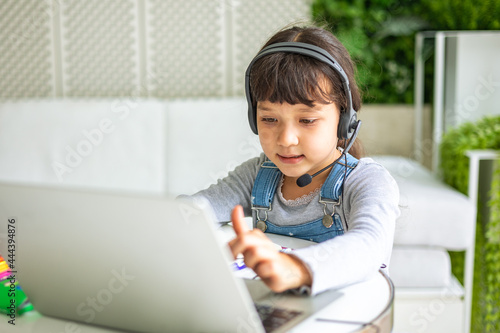 Small mixed race  girl sit at desk study online on laptop, smart little kid handwrite in notebook learning using internet lessons on quarantine, homeschooling concept. © anon