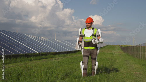 Man in exoskeleton walking in field near solar panels