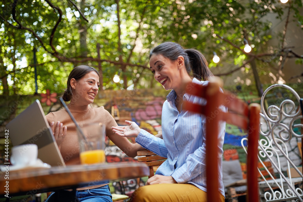 Two cheerful female friends having fun at a bar while watching a laptop content. Leisure, bar, friendship, outdoor Two cheerful female friends having fun at a bar while watching a laptop content. Leisure, bar, friendship, outdoor