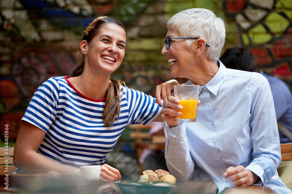 different age female friends concept. young woman laughing loud with elderly caucasian woman, sitting in outdoor cafe. different age female friends concept. young woman laughing loud with elderly caucasian woman, sitting in outdoor cafe.