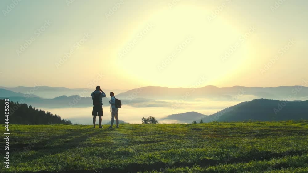 A man and a woman on top of a mountain meet the sunrise. Morning fog in a mountain valley. Beautiful landscape of the Ukrainian Carpathians for two tourists. A man and a woman on top of a mountain meet the sunrise. Morning fog in a mountain valley. Beautiful landscape of the Ukrainian Carpathians for two tourists.