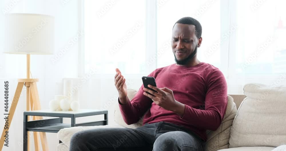 Man frustrated on receiving negative news using mobile phone at home Man frustrated on receiving negative news using mobile phone at home