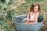 little cute girl in a pink swimsuit flops, having fun and splashing in a basin in the summer in the backyard, the concept of a happy childhood and summer vacation