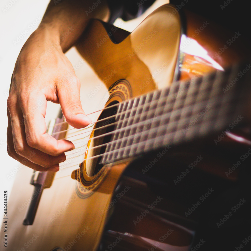 Fototapeta premium Hand of a musician playing an wooden acoustic guitar on a white and black background. Young guitar Player