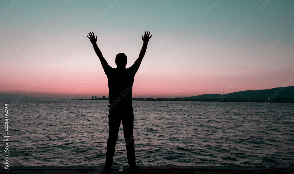 silhouette standing with both hands raised and sunset