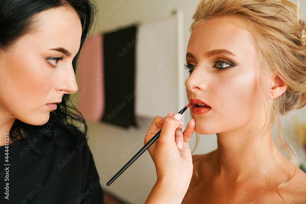 Professional female makeup artist applying cosmetics on model face use brush working at beauty salon. Woman visagist make up master dyeing facial visage to client appearance makeover