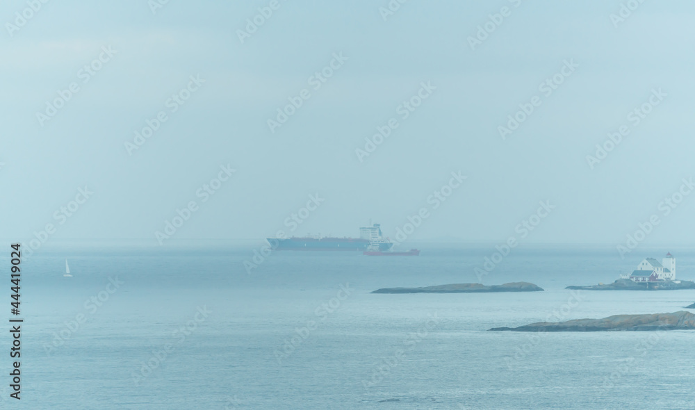 Large commercial cargo ships and sailboats sailing in dense fog near the shore.