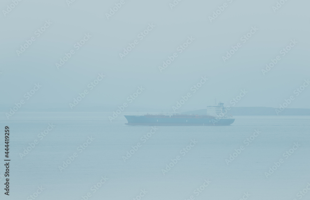 Large commercial cargo ship sailing in dense fog near the shore.