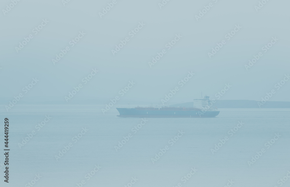 Large commercial cargo ship sailing in dense fog near the shore. Large commercial cargo ship sailing in dense fog near the shore.