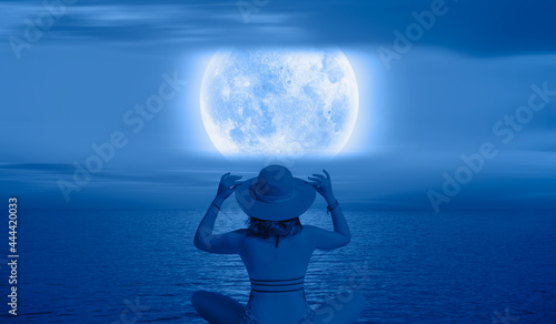 Fototapeta Naklejka Na Ścianę i Meble -  A beautiful young girl sitting by the sea and watching blue moon 