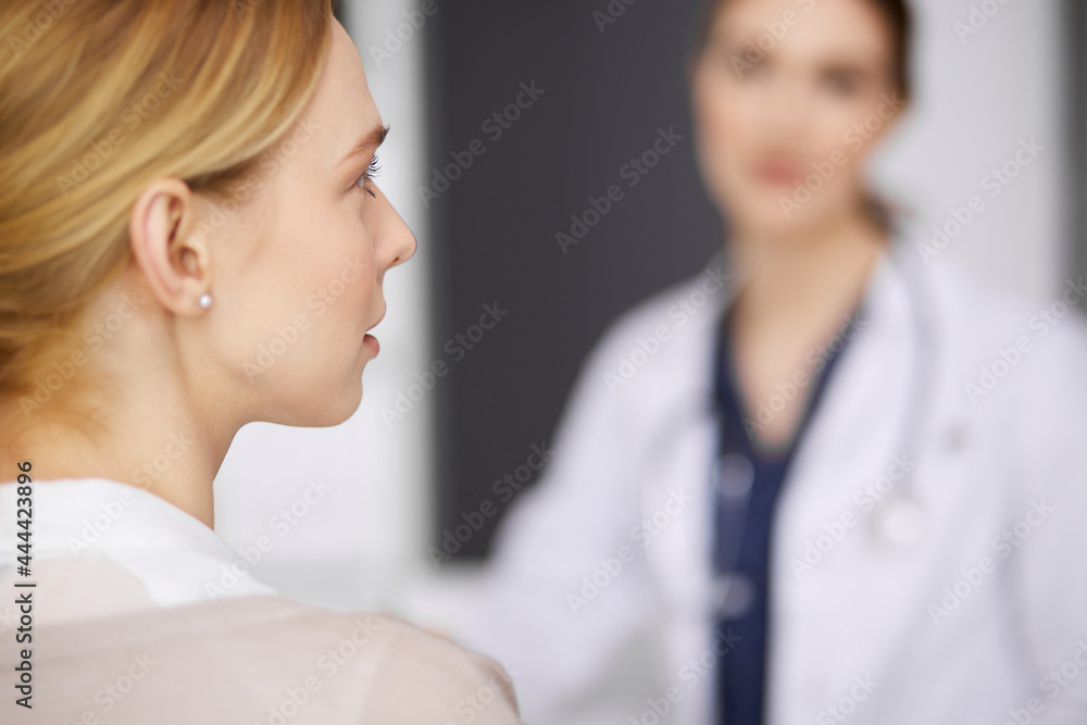 Friendly smiling female doctor and patient woman discussing current health examination while sitting in clinic. Perfect medical service in hospital. Medicine concept Friendly smiling female doctor and patient woman discussing current health examination while sitting in clinic. Perfect medical service in hospital. Medicine concept