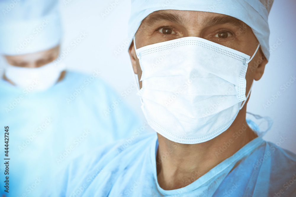 A male surgeon headshot, a group of surgeons is operating in the background. Health care concept A male surgeon headshot, a group of surgeons is operating in the background. Health care concept