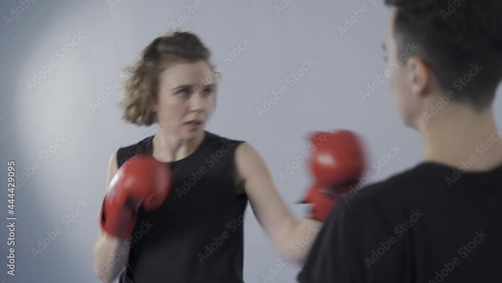 Martial art female theme. Sportswoman in red sports gloves practicing punches on paw held by personal Tekwando trainer in gym. Kickboxing workout and punching exercises with coach holding kick pad. Martial art female theme. Sportswoman in red sports gloves practicing punches on paw held by personal Tekwando trainer in gym. Kickboxing workout and punching exercises with coach holding kick pad.