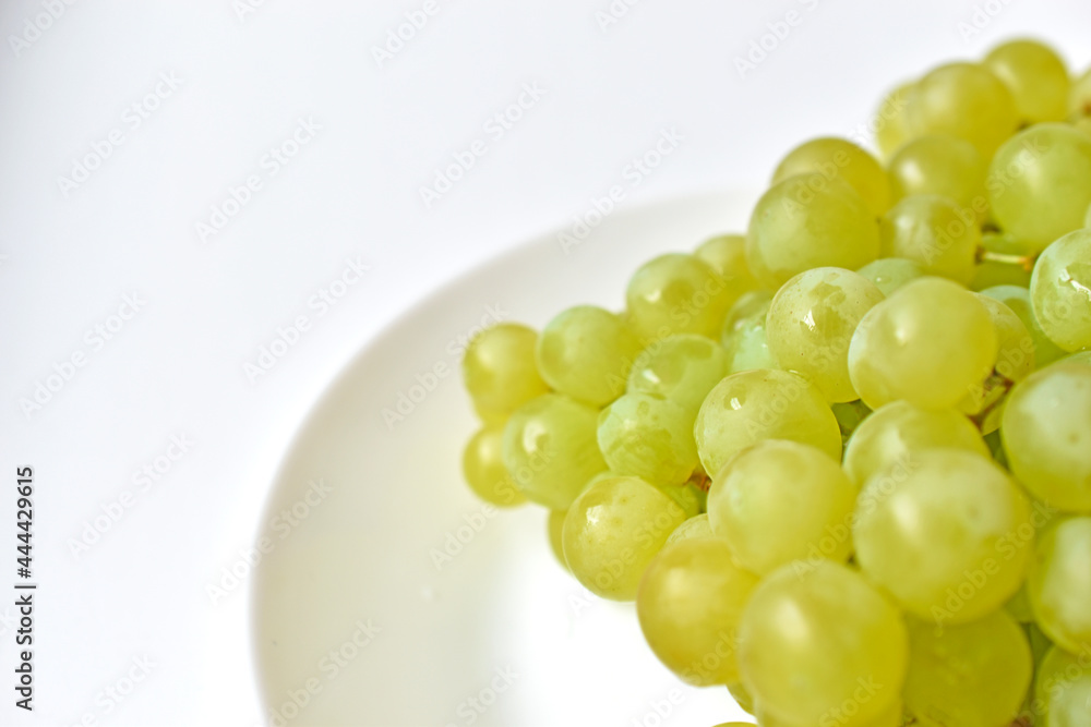 Green juicy delicious grapes on a white plate