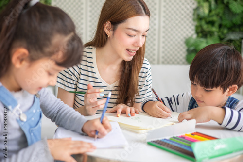 happy loving family. pretty young mother reading a book and drawing to her daughter and son.Mother teach Asian preschool student do homework by reawing by a color.