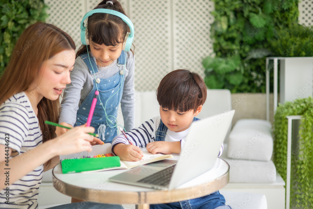 happy loving family. pretty young mother reading a book and drawing to her daughter and son.Mother teach Asian preschool student do homework by reawing by a color. happy loving family. pretty young mother reading a book and drawing to her daughter and son.Mother teach Asian preschool student do homework by reawing by a color.