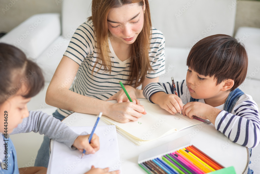 happy loving family. pretty young mother reading a book and drawing to her daughter and son.Mother teach Asian preschool student do homework by reawing by a color. happy loving family. pretty young mother reading a book and drawing to her daughter and son.Mother teach Asian preschool student do homework by reawing by a color.