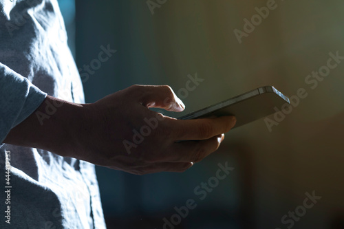 Close-up of man using mobile phone for searching information in internet. Persons hand holding smartphone on dark background.