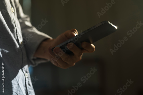 Close-up of man using mobile phone for searching information in internet. Persons hand holding smartphone on dark background.