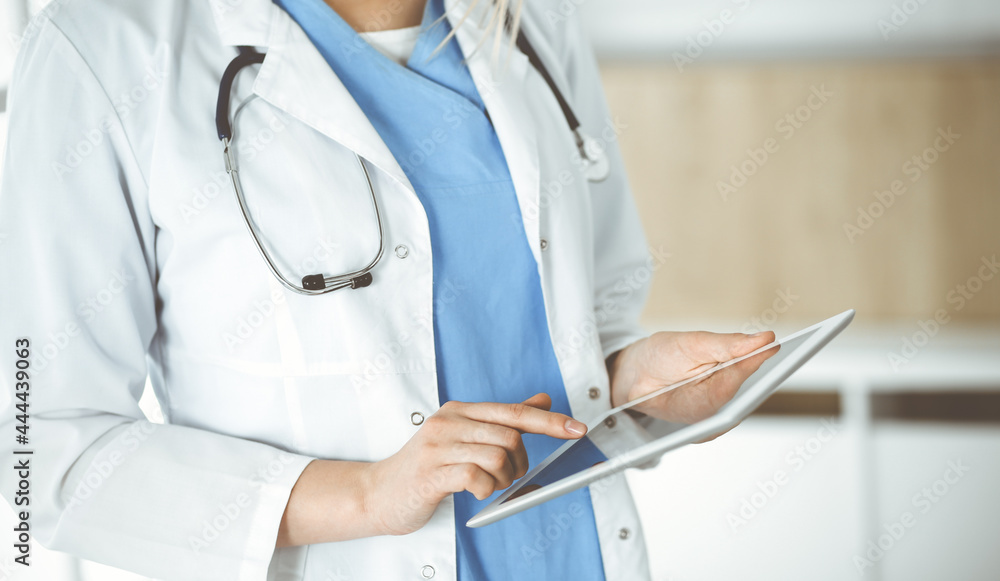 Unknown woman-doctor standing in clinic and using tablet pc, close-up. Data and best service in medicine and healthcare Unknown woman-doctor standing in clinic and using tablet pc, close-up. Data and best service in medicine and healthcare