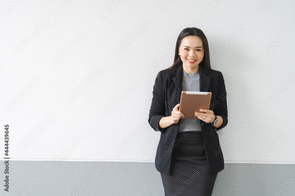 Portrait of a cheerful confident Asian businesswoman in a business suit standing whie using a digital tablet in the business building. Business stock photo Portrait of a cheerful confident Asian businesswoman in a business suit standing whie using a digital tablet in the business building. Business stock photo