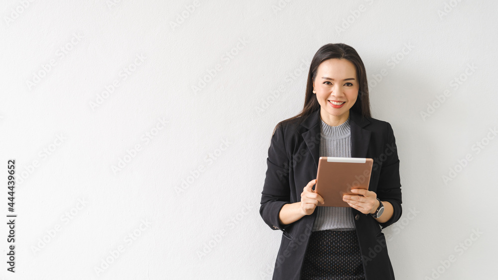 Portrait of a cheerful confident Asian businesswoman in a business suit standing whie using a digital tablet in the business building. Business stock photo Portrait of a cheerful confident Asian businesswoman in a business suit standing whie using a digital tablet in the business building. Business stock photo