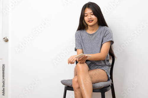 Beautiful young Asian woman smiling sitting relax in the room, using smart phone on white background.