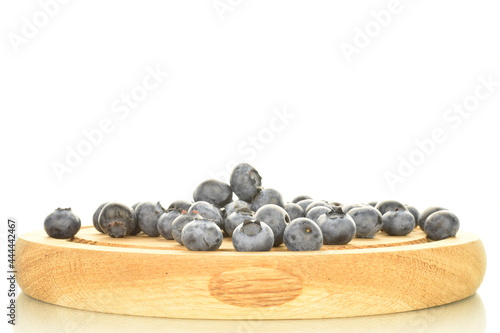 Several berries of ripe dark purple blueberries on a round tray made of wood  close-up  isolated on white.