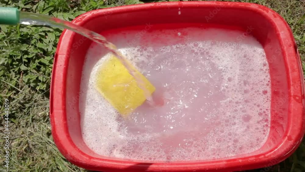 A housewife pouring water from a hose into a soapy liquid in a red