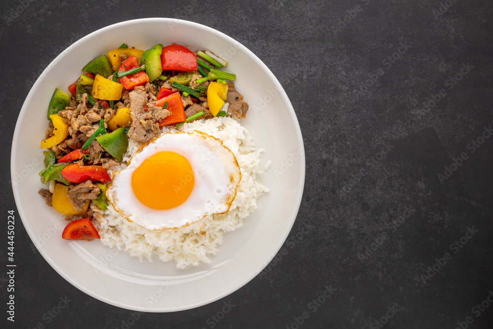 streamed rice topped with stir fried beef with black pepper, red, yellow, green sweet pepper, bell pepper or capsicum, spring onion and egg in ceramic plate on dark tone texture background, top view streamed rice topped with stir fried beef with black pepper, red, yellow, green sweet pepper, bell pepper or capsicum, spring onion and egg in ceramic plate on dark tone texture background, top view
