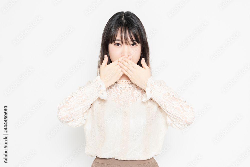 白背景の前に立って、口を隠す、レースのブラウスを着た若い女性 白背景の前に立って、口を隠す、レースのブラウスを着た若い女性