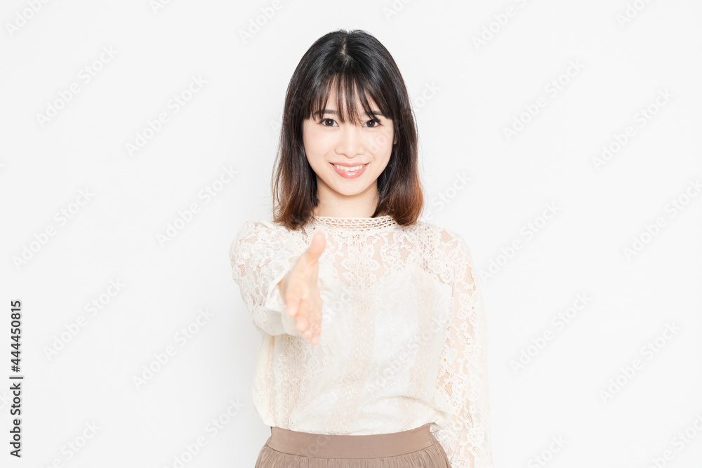 白背景の前に立って、握手のジェスチャーをする、レースのブラウスを着た若い女性 白背景の前に立って、握手のジェスチャーをする、レースのブラウスを着た若い女性