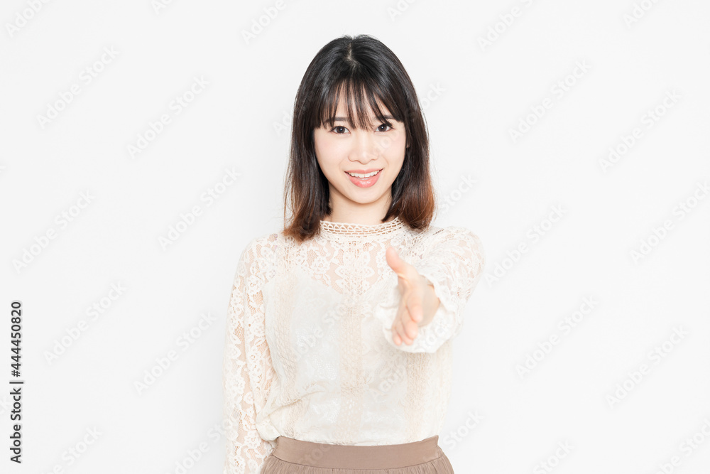 白背景の前に立って、握手のジェスチャーをする、レースのブラウスを着た若い女性