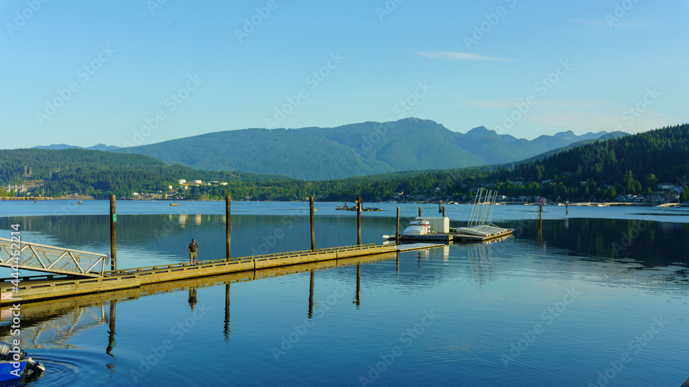 Jetty and posts reflected in calm waters of Burrard Inlet, BC, early morning, with mountain backdrop