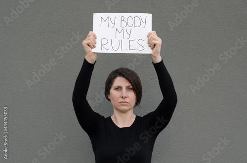Murais de parede Adult brunette woman with short hair holding banner above her head with My Body My Rules message