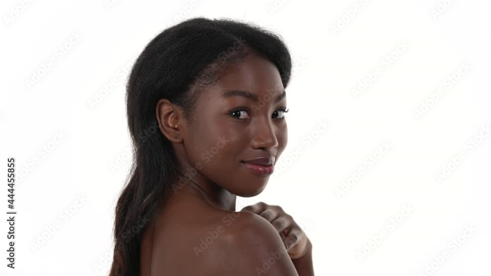 Side view of a beautiful African woman, touching her skin and smiling to the camera. White background. Side view of a beautiful African woman, touching her skin and smiling to the camera. White background.