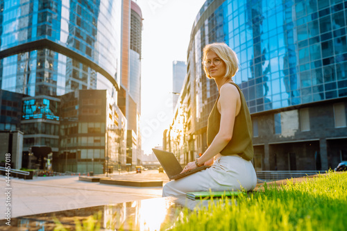 Blonde business woman wearing glasses sit with laptop among the skyscrapers © Olga