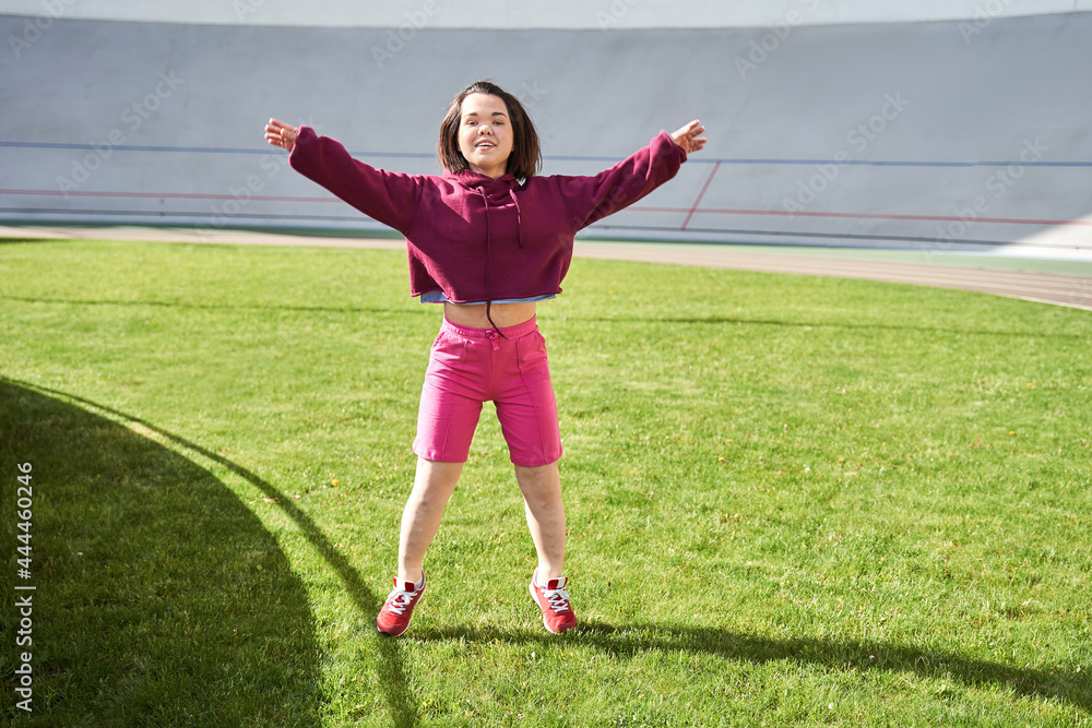 Dwarf woman doing stretching at the sports stadium while smiling widely and rejoicing