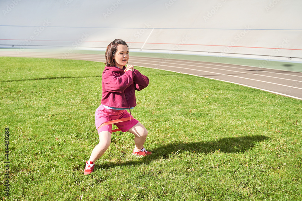 Midget girl with perfect body practicing squats with elastic bands outdoors Midget girl with perfect body practicing squats with elastic bands outdoors