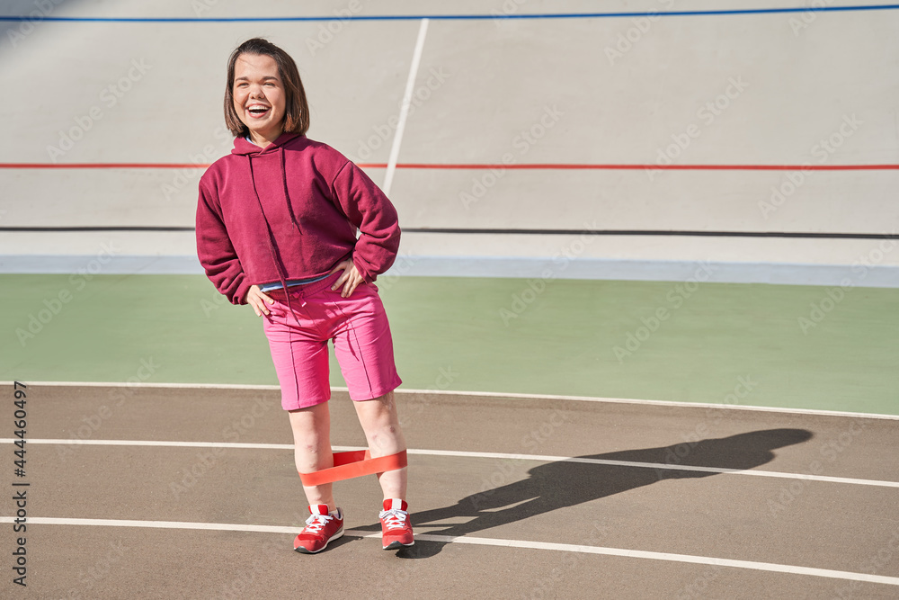 Dwarf woman laughing out loud while training at the sunny morning with elastic bands
