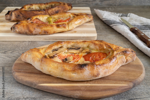 Peinirli with varied flavours baked and ready to serve. Three Greek open faced pizzas on different cutting boards placed on kitchen surface with towel and cutlery.