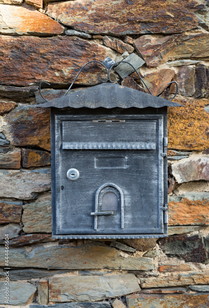 an antique gray and metallic mailbox hanging on a stone wall