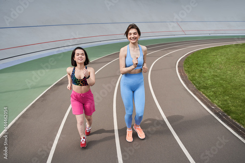 Women in sports outfits jog on running track in city stadium in sunny morning